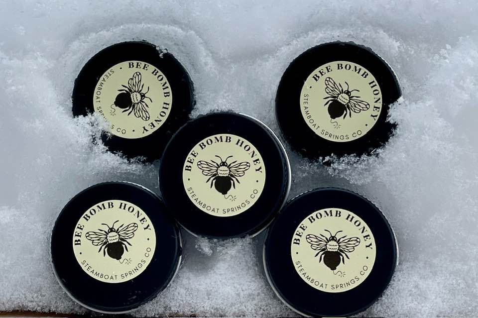 Five Bee Bomb Honey lip balm tins arranged in snow