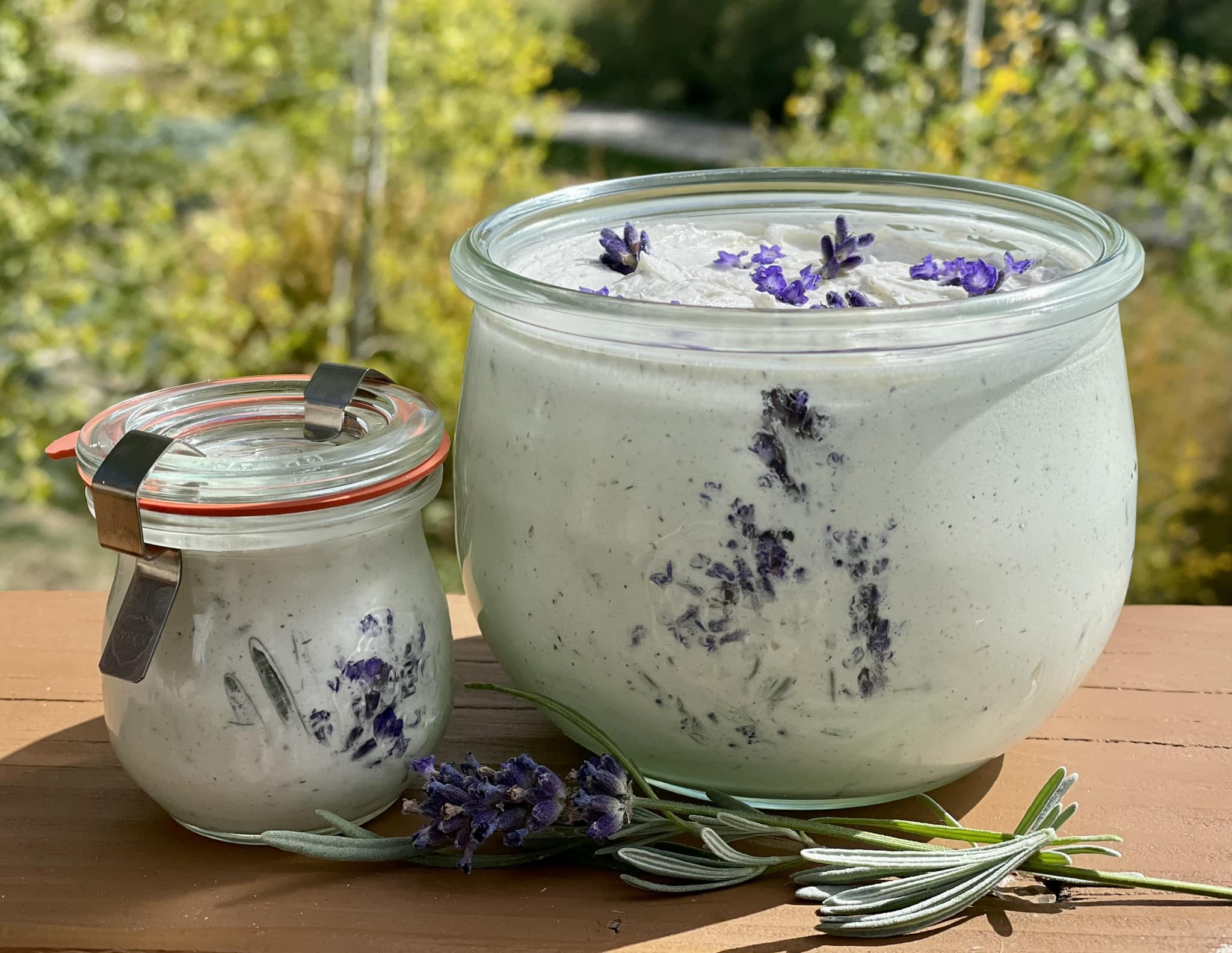Two glass jars of lavender honey butter with fresh lavender sprigs on a wooden deck