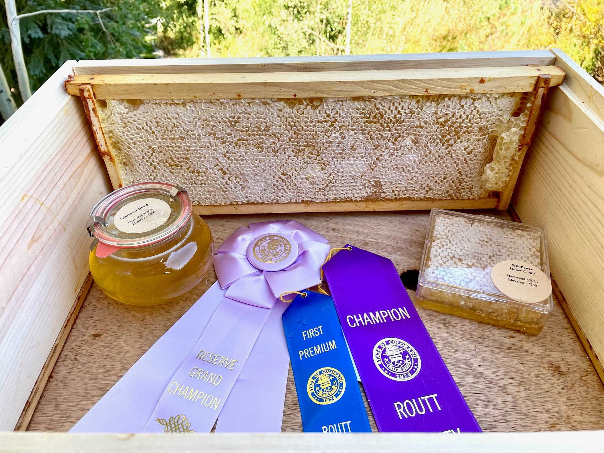 Honey jar, honeycomb, and competition ribbons arranged in a wooden crate